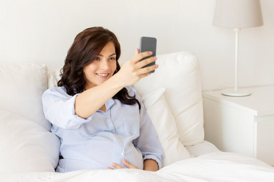 pregnant woman taking smartphone selfie at home