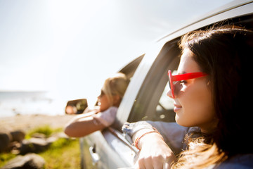 happy teenage girls or women in car at seaside
