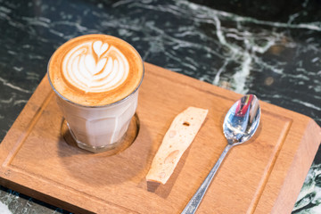 A cup of coffee with latte art serve with some biscuits
