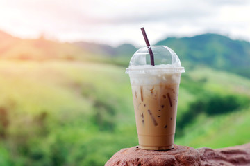 Closeup ice coffee in plastic cup with beautiful mountain background.