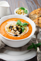Homemade pumpkin soup with cream, fresh bread and basil on rustic wooden background, selective focus