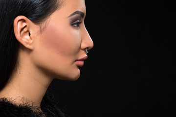 Fototapeta premium Closeup profile of brunette model woman demonstrating her perfect makeup in studio. Beautiful lady posing isolated on black background.
