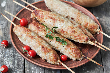 Grilled kebabs on wooden skewers and fresh vegetables on a plate close-up. horizontal