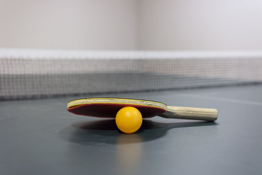 Table tennis racquet on the table with the network and ball.
