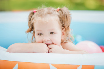 The little baby girl playing with toys in inflatable pool in the summer sunny day