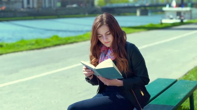 Woman receives message on smartphone while reading book on the bench
