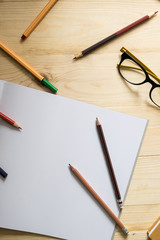 blank paper and colorful pencils and glasses on old wooden table with mornning light.