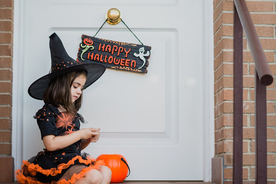 Cute little witch looking at her hands in front of door