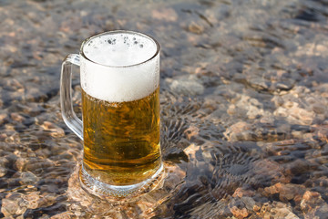 Mug fresh beer sparkles on the stone in river