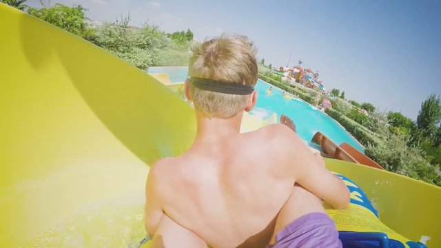 Two guys on the family water slide going down in slow motion