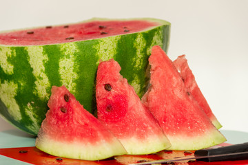 Спелый, сочный арбуз и несколько долек арбуза на светлом фоне. Здоровое питание.