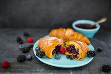 Delicious croissants and ripe berries on stone background.