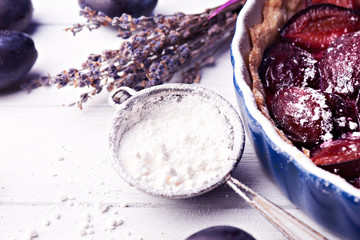 Sieve with sugar powder and part of plum pie