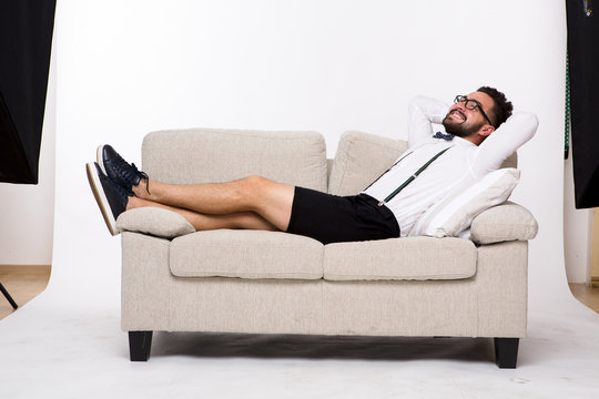 Picture of happy or cheerful smiling handsome man lying on couch or sofa. Young man in glasses posing isolated on white background in studio.