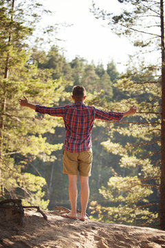 Young man enjoing fresh air in forest standing 
arms spread wide