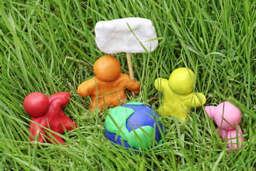 Plasticine globe in tall grass. Modelling clay peoples hold a placard. The concept of Earth Day.