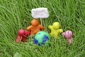 Fototapeta premium Plasticine globe in tall grass. Modelling clay peoples hold a placard. The concept of Earth Day.