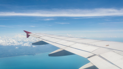 Fototapeta premium Wing of a plane from window view with bright blue sky and sea background.