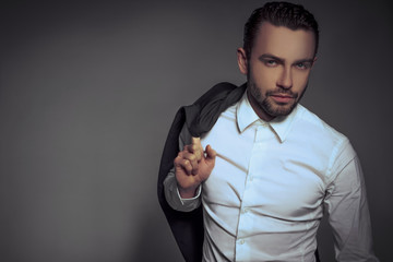 Young handsome man holding a jacket posing isolated over gray background