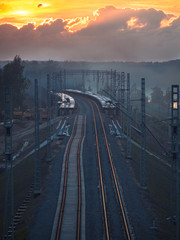 Toned image of the railway with sleepers and rail bridge on a background of multicolored sunset with clouds in the sky