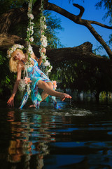 Girl on home made tree swing over river. Swing decorated with flowers. Woman with flower wreath on head.