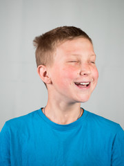 Portrait of laughing boy with eyes closed on a gray background