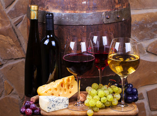 Red, rose and white glasses and bottles of wine with grapes in wine cellar. Grape, nuts, cheese and old wooden barrel