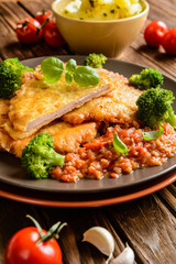 Piccata - fried pork cutlets stuffed with smoked ham slices coated in cheese and eggs served with tomato sauce, steamed broccoli and boiled potatoes