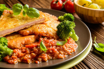 Piccata - fried pork cutlets stuffed with smoked ham slices coated in cheese and eggs served with tomato sauce, steamed broccoli and boiled potatoes
