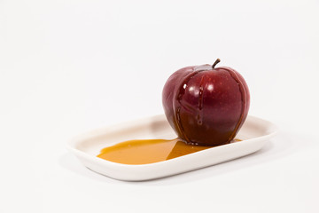 Red apple with drops of honey on white plate with honey isolated on a white background