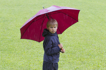 Boy under an umbrella in the rain. Outdoors.