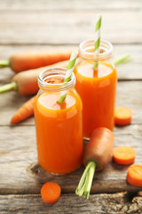Fresh carrot juice in bottles on a grey wooden table