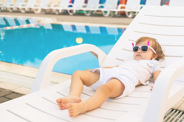 Endless summer! Cute baby relaxing at sunbed near pool, resort.