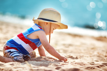 little boy playing at the beach in straw hat