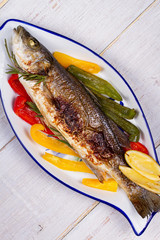 Whole grilled seabuss fish with colorful peppers, lemon and rosemary. View from above, top studio shot