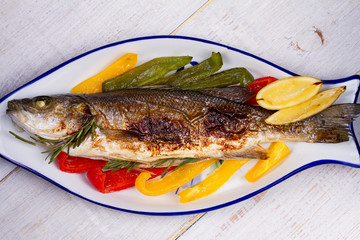 Whole grilled seabuss fish with colorful peppers, lemon and rosemary. View from above, top studio shot