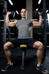 Fototapeta na wymiar Muscular man doing dumbbell overhead press in the gym