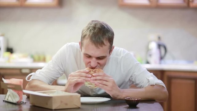 Handsome man chewing and enjoying a hamburger with fries at home