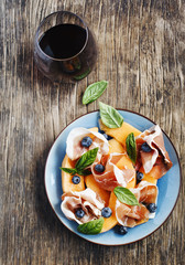Sliced prosciutto with melon, basil leaves and blueberries serve