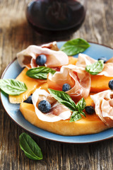 Sliced prosciutto with melon, basil leaves and blueberries serve