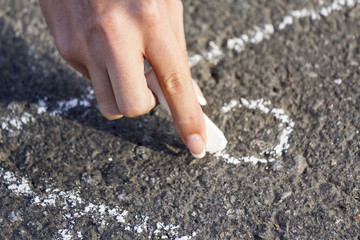 Hand girl draws by a chalk roof House on the sidewalk