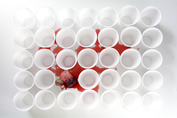 bleeding teabag with red tea between rows of white plastic cups, abstract art concept of social issues