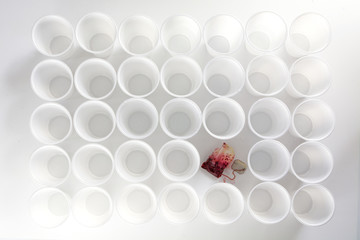 red used teabag between ordinary rows of white plastic cups, outsider concept, abstract art style