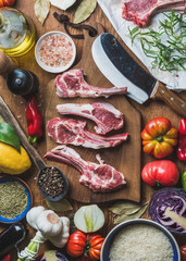 Ingredients for cooking dinner. Raw uncooked lamb meat ribs, rice, oil, spices and vegetables over wooden background, top view, vertical composition