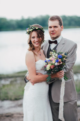 young groom and bride standing hugging on the background of the river