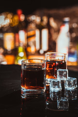 two glasses of whiskey on a blurred background bar