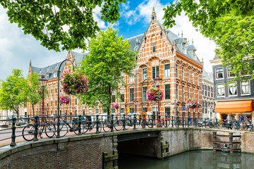 Typical canal side cityscape of Amsterdam, opposite from the 17th century HQ of the Dutch East India Company, now used by the University of Amsterdam - obrazy, fototapety, plakaty