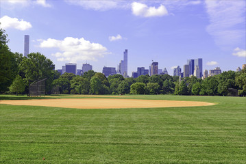 Fototapeta na wymiar Green grass and baseball field of Central Park with Manhattan skyline and blue sky