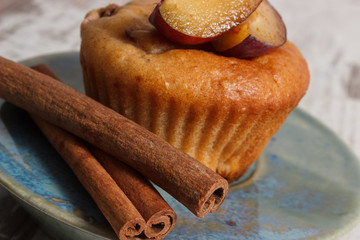 Fresh baked muffins with plums and cinnamon sticks on old wooden background, delicious dessert