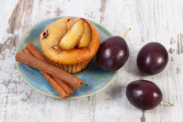 Fresh baked muffins with plums and cinnamon sticks on old wooden background, delicious dessert
